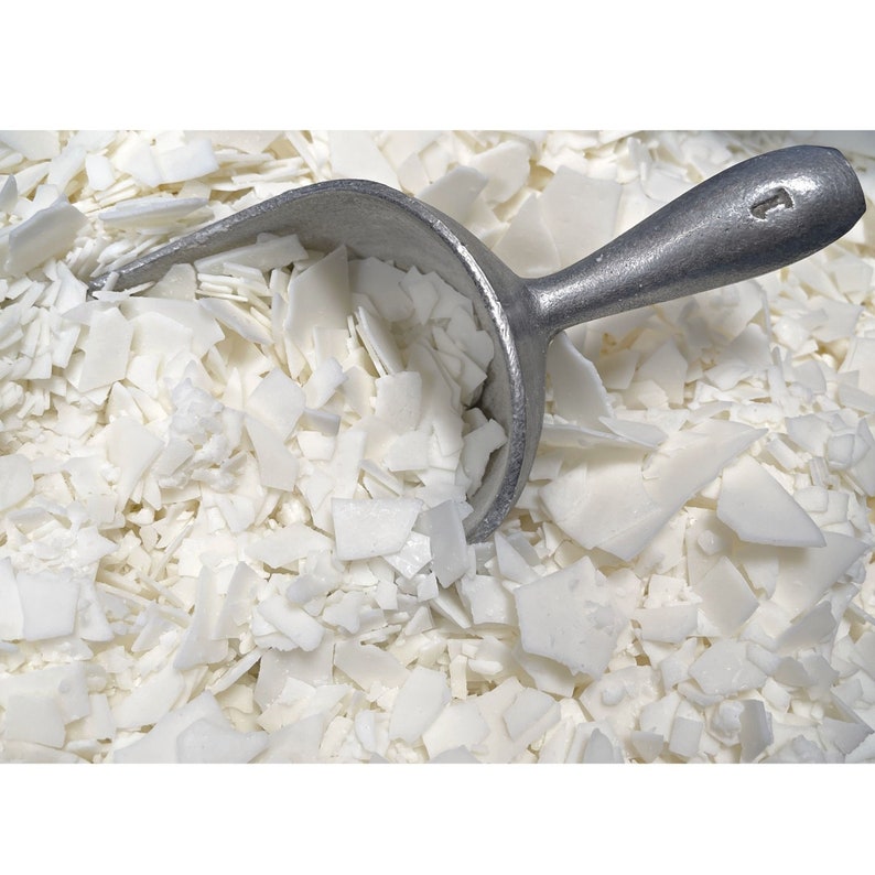 May include: A close-up of a white wax flakes with a silver scoop. The wax flakes are used for making candles.