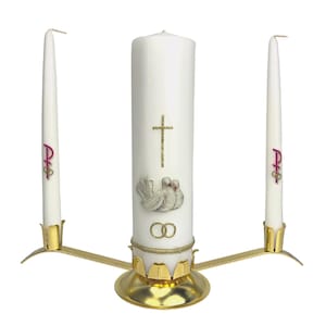 Puede incluir: Un juego de velas de unidad de boda blancas con dos velas más pequeñas y un soporte de metal dorado. La vela central presenta una paloma con dos anillos y una cruz. Las velas más pequeñas tienen el símbolo "P+S" en ellas.