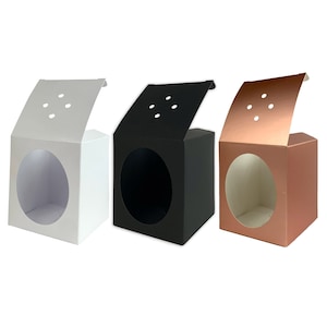 May include: Three gift boxes with lids open, showing a round window. The boxes are white, black, and rose gold.