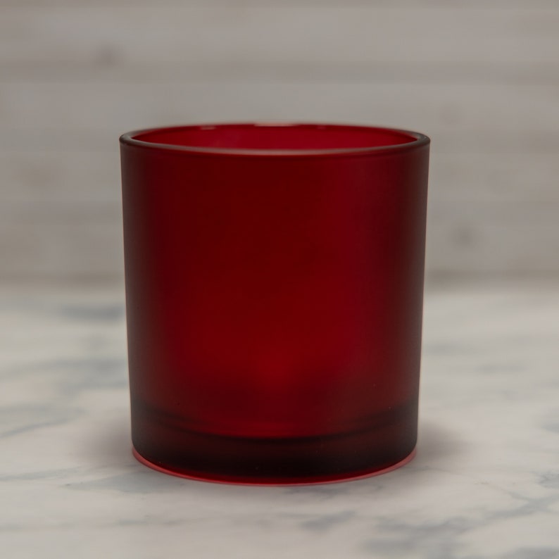 May include: A red glass candle jar with a frosted finish. The jar is empty and ready to be filled with wax and a wick.