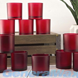 May include: Ten red glass candle jars, frosted and opaque, arranged in a pyramid shape on a wooden crate. The jars are empty and ready to be filled with wax and wicks.