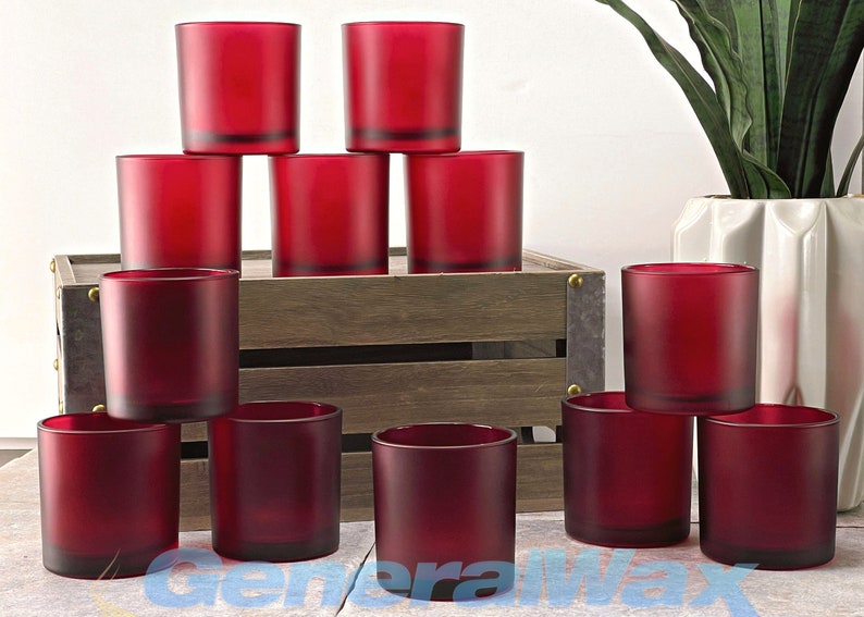 May include: Ten red glass candle jars, frosted and opaque, arranged in a pyramid shape on a wooden crate. The jars are empty and ready to be filled with wax and wicks.