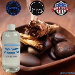Könnte beinhalten: Eine durchsichtige Glasflasche mit einem weißen Etikett, auf dem "GeneralWax High Quality Fragrance Oil 16 oz. (473.176 ml)" steht. Die Flasche steht auf einer Holzoberfläche mit einem braunen und weißen Räucherstäbchen, schwarzen Steinen und einem "Made in the U.S.A." Aufkleber.