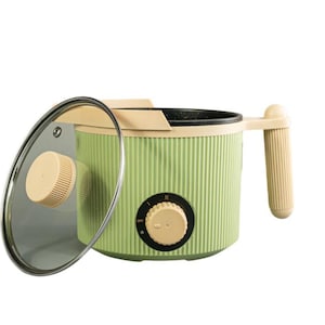 Puede incluir: Una olla eléctrica verde claro y beige con tapa de cristal. La olla tiene un diseño acanalado, un asa beige y un mando de control. La tapa está parcialmente abierta, revelando el interior. Diseñada para cocinar.