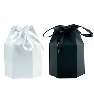May include: Two hexagonal gift boxes, one white and one black, are shown against a white backdrop. Each box is tied with a satin ribbon in a matching colour. The boxes have a geometric design.