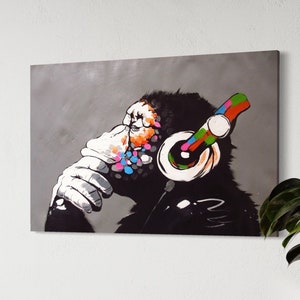 May include: A canvas print depicting a chimpanzee wearing headphones. The chimpanzee's face is partially covered with a white hand, and colourful paint splatters adorn its face. The headphones have a rainbow-coloured band.