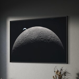 May include: A framed monochrome photograph of the moon, displaying its cratered surface and a crescent. The artwork is mounted on a grey wall above a wooden cabinet. A desk, chair, and lamp are in the foreground.