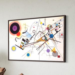 Puede incluir: Impresión de arte abstracto en un marco de madera oscura. La obra presenta una compleja disposición de formas geométricas, líneas y círculos en varios colores, incluyendo negro, rojo, amarillo y azul, sobre un fondo blanco. El estilo recuerda al expresionismo abstracto de principios del siglo XX.