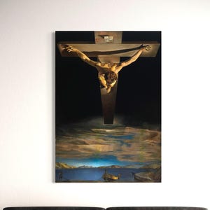 May include: A framed canvas print of a surrealist painting depicting a figure on a cross suspended above a landscape. The artwork features a dark background, a wooden cross, and a detailed depiction of a body. The landscape includes a body of water and a boat.