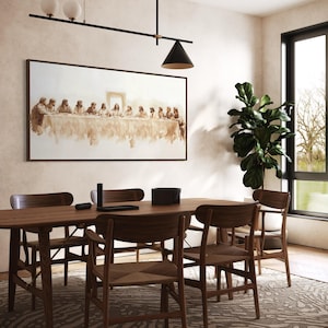 May include: A dining room scene with a wooden table and chairs. A framed artwork depicting a religious scene hangs above the table. A large potted plant is near a window, and a modern light fixture hangs from the ceiling.