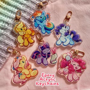 May include: Six colourful epoxy acrylic keychains featuring My Little Pony characters. The keychains are clear and have glitter inside. The characters are Twilight Sparkle, Pinkie Pie, Rainbow Dash, Fluttershy, Rarity, and Applejack.