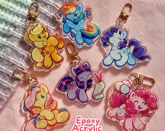 May include: Six colorful epoxy acrylic keychains featuring My Little Pony characters. The keychains are clear and have glitter inside. The characters are Twilight Sparkle, Pinkie Pie, Rainbow Dash, Fluttershy, Rarity, and Applejack.