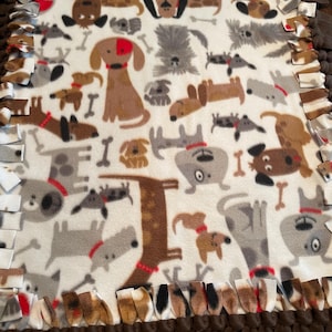 May include: A white fleece blanket with a brown and white knotted fringe border. The blanket features a repeating pattern of cartoon dogs in various poses and colors.