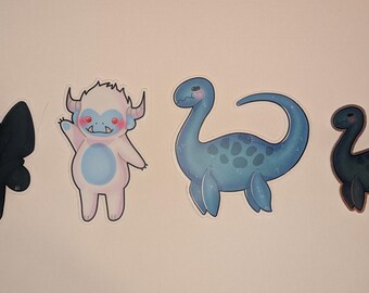 Puede incluir: Cuatro pegatinas de dibujos animados coloridos con una polilla negra, un yeti blanco, un dinosaurio azul y un dinosaurio negro.