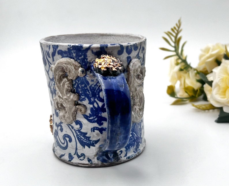 May include: A white ceramic mug with a blue and white floral pattern, a blue handle, and gold accents.