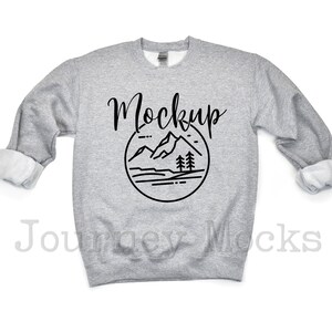 May include: Gray sweatshirt with a black mountain and tree graphic and the word "Mockup" in a handwritten font.