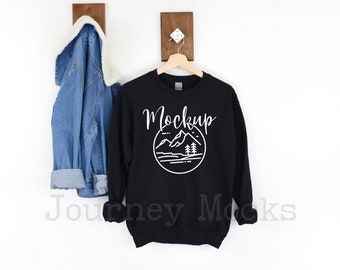 May include: Black sweatshirt with a white graphic of mountains and trees in a circle. The text "Mockup" is above the graphic.