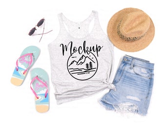 May include: A gray tank top with a black mountain graphic and the word "Mockup" printed on it. The tank top is laid flat on a white surface with a straw hat, denim shorts, flip flops, and sunglasses.