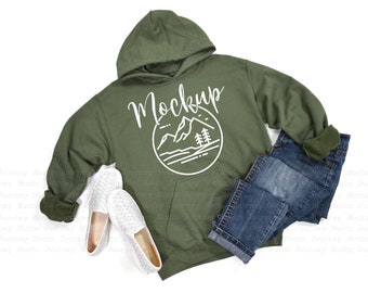 May include: A green hooded sweatshirt with a white graphic of a mountain range and trees inside a circle. The text "Mockup" is written above the graphic.