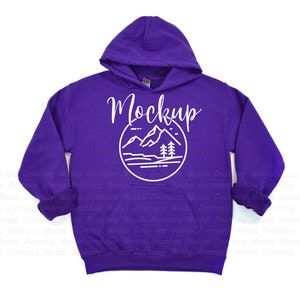 May include: Purple youth-sized hooded sweatshirt with a white graphic of a mountain range and trees inside a circle. The text "Mockup" is above the graphic.