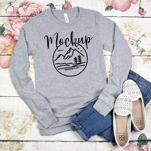 May include: A heather gray long-sleeve shirt with a black mountain graphic and the word "Mockup" in a handwritten font.