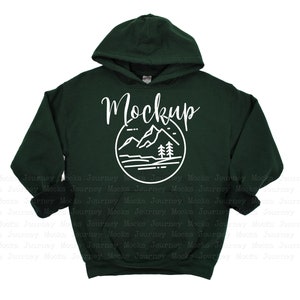 May include: A dark green hooded sweatshirt with a white graphic of a mountain range and trees inside a circle. The text "Mockup" is written above the graphic.