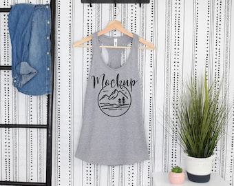 May include: Gray tank top with a black mountain graphic and the word "Mockup" printed on the front. The tank top is hanging on a wooden hanger against a white and black patterned background.