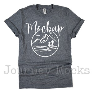 May include: A dark heather grey t-shirt with a white graphic of mountains and trees. The text "Mockup" is printed in white on the shirt.