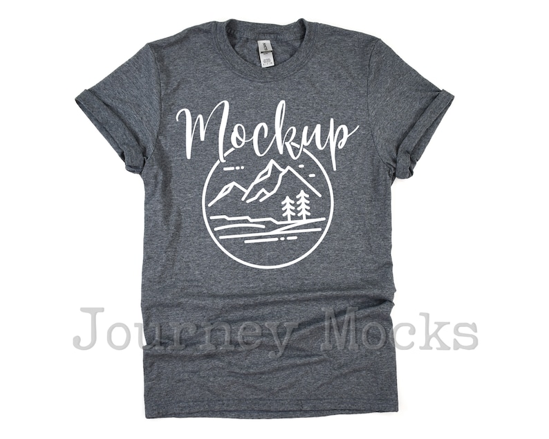 May include: A dark heather grey t-shirt with a white graphic of mountains and trees. The text "Mockup" is printed in white on the shirt.