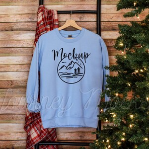 May include: Light blue sweatshirt with a black mountain and trees graphic and the word "Mockup" in black text.