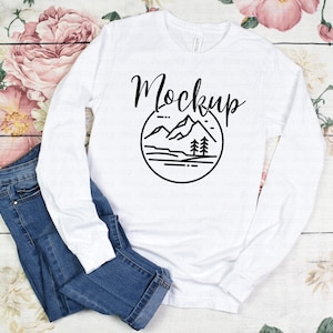 May include: White long-sleeve shirt with a black mountain scene graphic and the word "Mockup" in cursive.