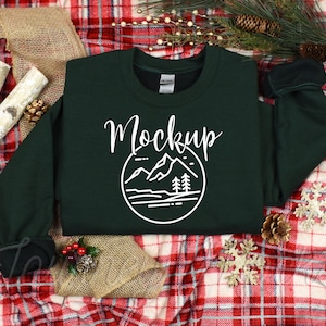 May include: A dark green sweatshirt with a white graphic of mountains and trees in a circle. The text "Mockup" is written above the graphic.