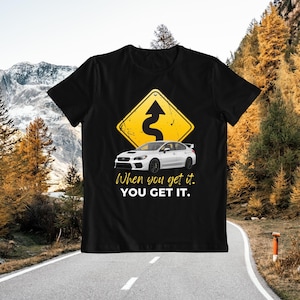 May include: Black t-shirt with a white Subaru WRX STI car and a yellow warning sign with a winding road graphic. The text "When you get it. YOU GET IT." is printed below the car.