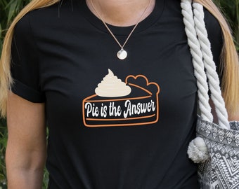 May include: Black t-shirt featuring a pie slice graphic with whipped cream and the text "Pie is the Answer" in an orange and white design. The shirt has short sleeves and a crew neck.