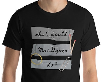 May include: Black t-shirt with the phrase "what would MacGyver do?" in handwritten style. The design includes a match, a paperclip, and a rubber band, all taped to the shirt with gray tape.