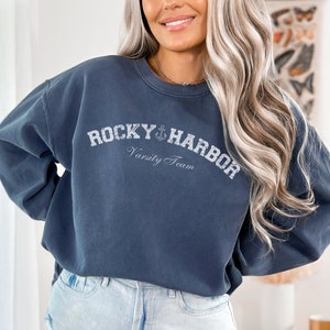 May include: A navy blue sweatshirt with a white graphic that says "Rocky Harbor Varsity Team" with an anchor symbol.