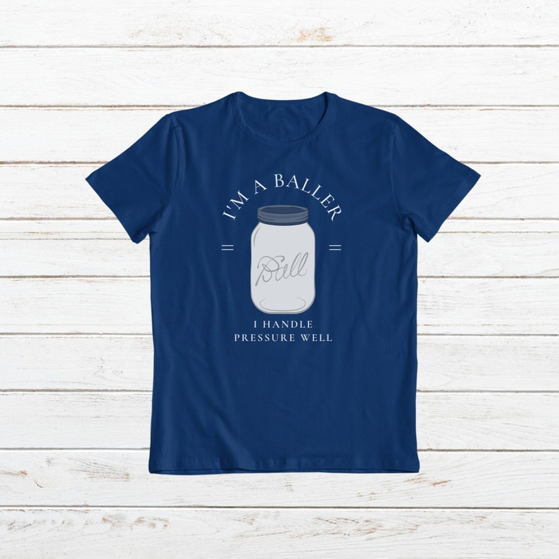 Puede incluir: Una camiseta azul marino con un gr&aacute;fico blanco de un frasco de vidrio con la palabra "Ball" en su interior. El texto "I'm a Baller" est&aacute; por encima del frasco y "I handle pressure well" est&aacute; por debajo del frasco.