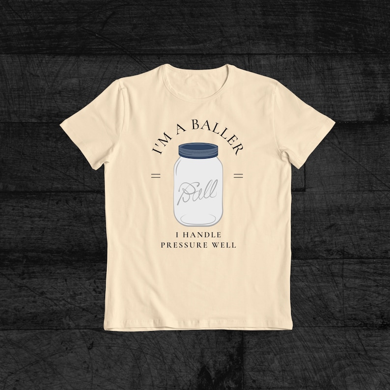 Puede incluir: Una camiseta beige con un gr&aacute;fico de un frasco de vidrio con el texto "I'm a Baller" y "I handle pressure well".