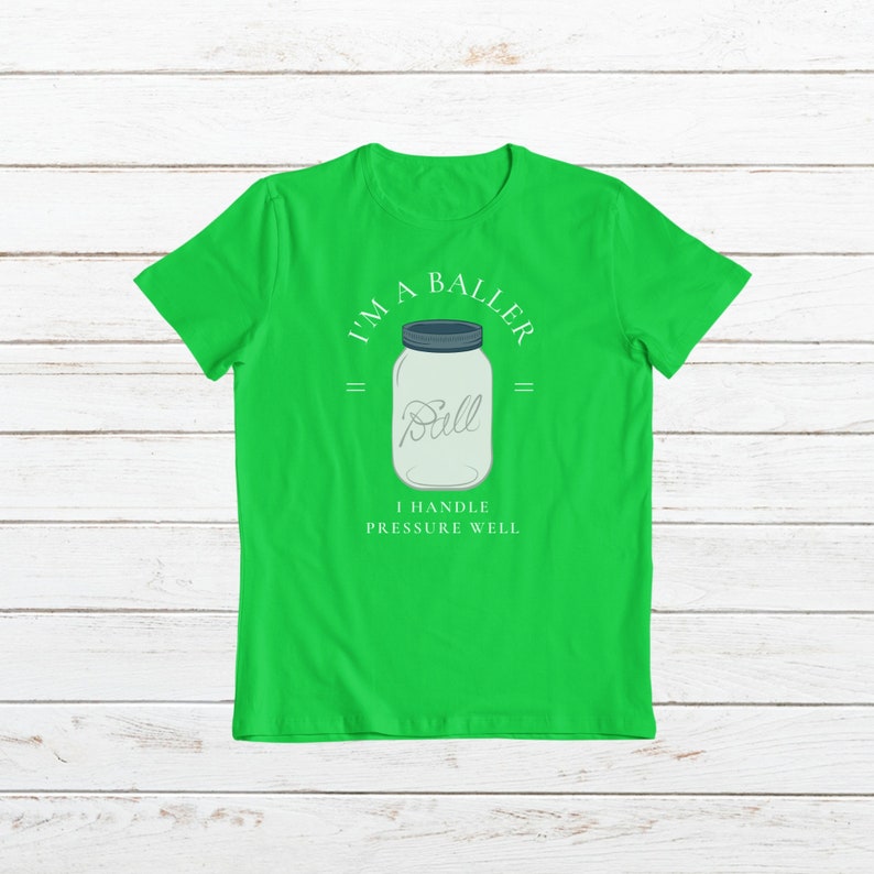 Puede incluir: Camiseta verde con un tarro de cristal blanco con la palabra "Ball" en su interior. El texto "I'm a Baller" est&aacute; por encima del tarro y "I handle pressure well" est&aacute; por debajo del tarro.