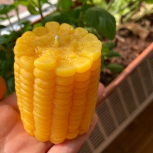 May include: A yellow candle shaped like an ear of corn with a white wick.
