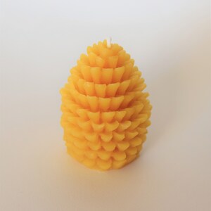 May include: A yellow beeswax candle shaped like a pine cone.