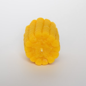 May include: A yellow corn on the cob candle. The candle is made to look like a real ear of corn with rows of kernels.