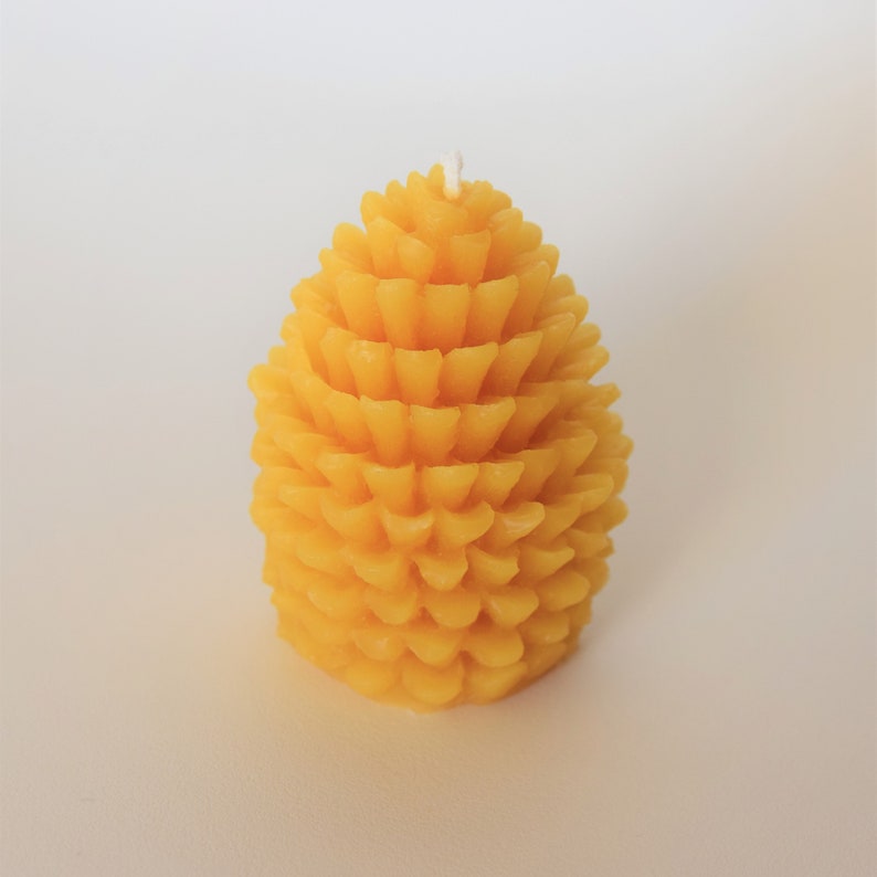 May include: A yellow beeswax candle shaped like a pine cone.
