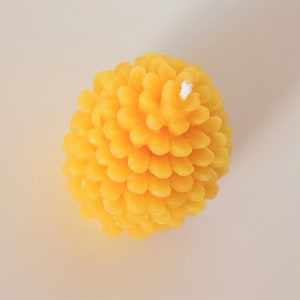 May include: A yellow beeswax candle shaped like a pine cone with a white wick.