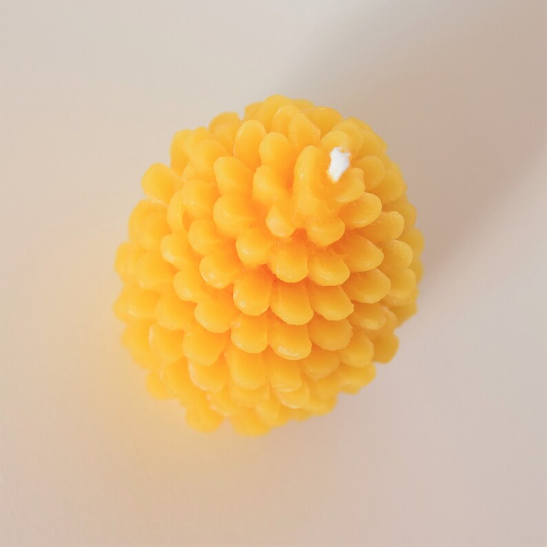 May include: A yellow beeswax candle shaped like a pine cone with a white wick.