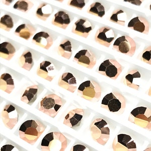 May include: A close-up view of a sheet of rose gold rhinestones in a white plastic tray. The rhinestones are arranged in rows and columns, and they are all the same size and shape.