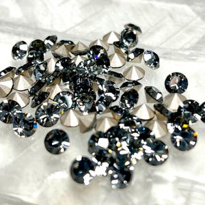 May include: A large pile of black and silver rhinestones. The rhinestones are scattered on a white surface.