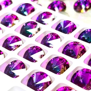 Puede incluir: Una vista cercana de una bandeja llena de piedras preciosas ovaladas de color púrpura iridiscente. Las piedras preciosas están dispuestas en un patrón de cuadrícula y tienen una variedad de tonos de púrpura.