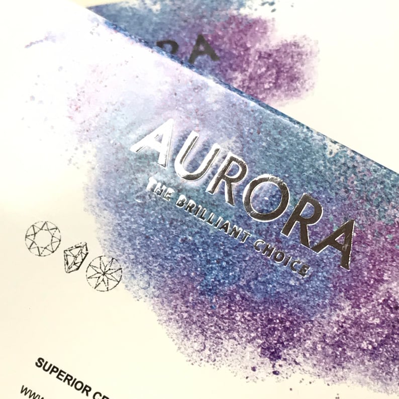 May include: A white box with a silver foil design that says "Aurora The Brilliant Choice" with a watercolor background of purple and blue. The box also has two small diamond illustrations.