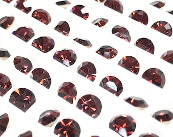 May include: A close-up view of a tray of loose, faceted, dark red gemstones. The gemstones are arranged in rows on a white background.